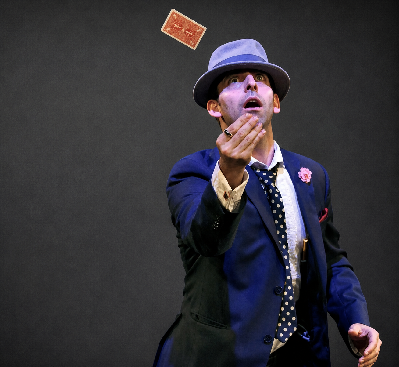 Naz Magic performing a card flourish on stage in a suit
