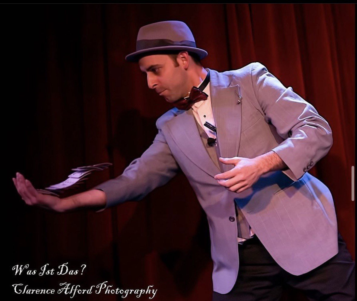 Naz Magic performing on a lit stage in a suit and hat