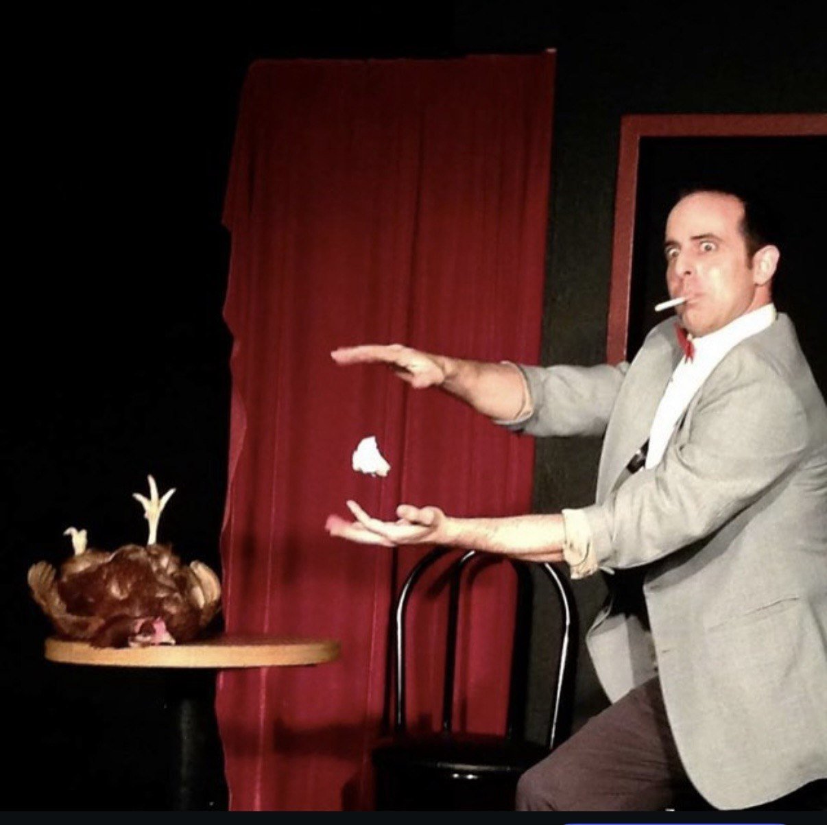 Naz Magic performing a magic routine on a red-curtained stage